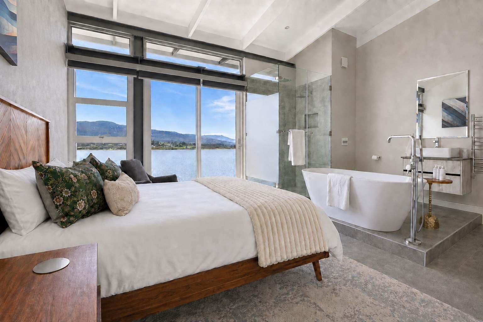A modern bedroom with a large bed, a bathtub, and a view of a lake.