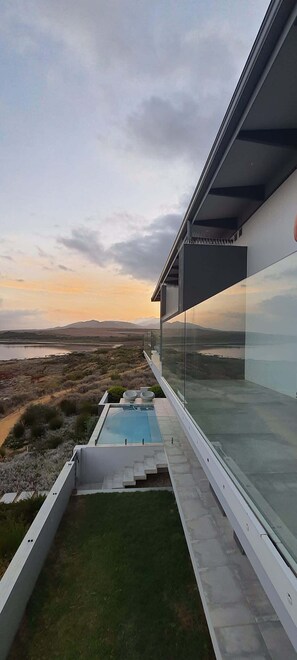 Ein moderner Poolbereich im Freien mit Glaswänden, Blick auf die Landschaft und einem Sonnenuntergang im Hintergrund.
