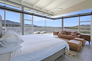 Ein modernes Schlafzimmer mit einem großen Bett, einer Couch und Blick auf einen See und Berge.