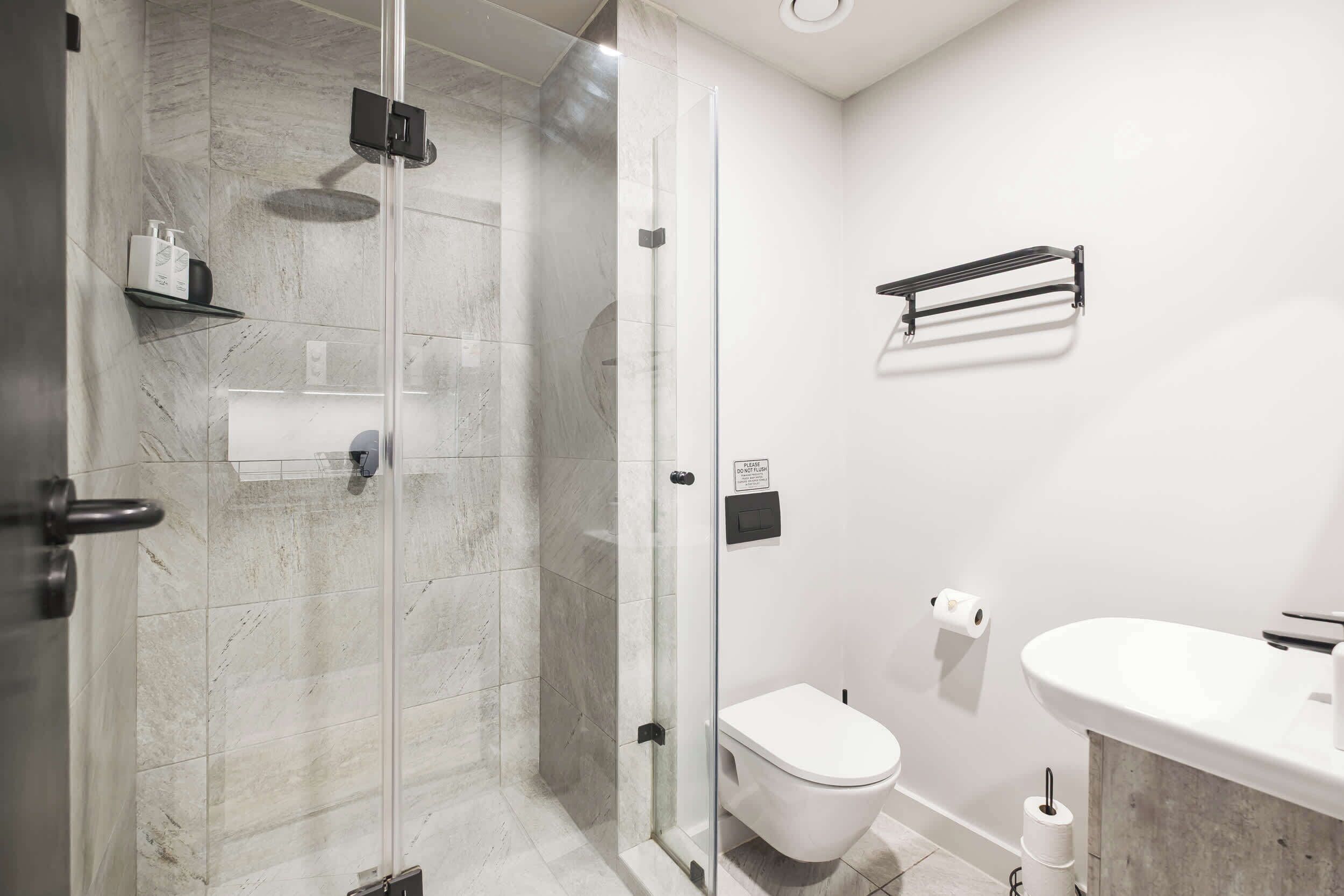 Une salle de bain moderne avec une douche à parois de verre, des toilettes blanches, un lavabo et un porte-serviettes.