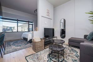 Ein modernes Wohnzimmer mit Bett, Fernseher, Sofa und großen Fenstern.