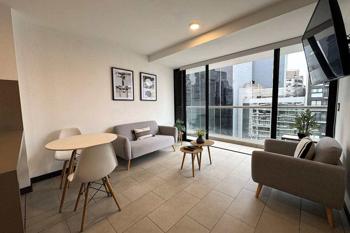 A modern living room with a sofa, chairs, a small table, and artwork on the wall.