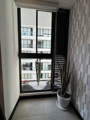 Una habitación con un ventanal grande, una planta en maceta y un papel tapiz estampado.