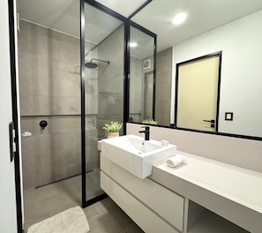 A modern bathroom with a glass shower enclosure, a white sink, and a large mirror. - Aparts4Days 1 Bedroom Apartment 548 (San Isidro)