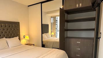Une chambre d’hôtel avec un grand lit, une table de chevet avec une lampe, une armoire avec de nombreux tiroirs et un miroir qui reflète la pièce.