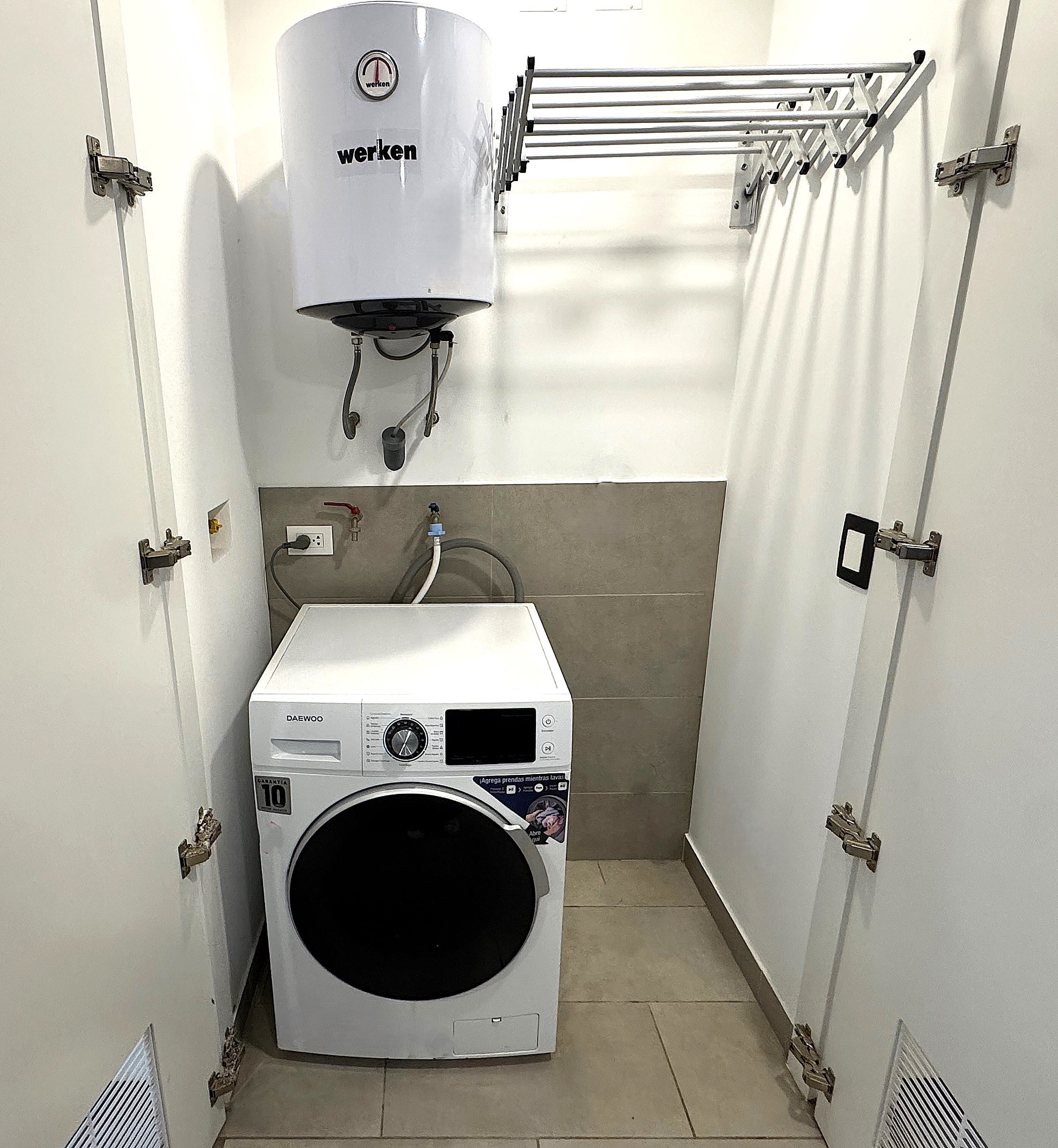 Une petite buanderie équipée d’un lave-linge à chargement frontal, d’un radiateur mural et d’un étendoir.