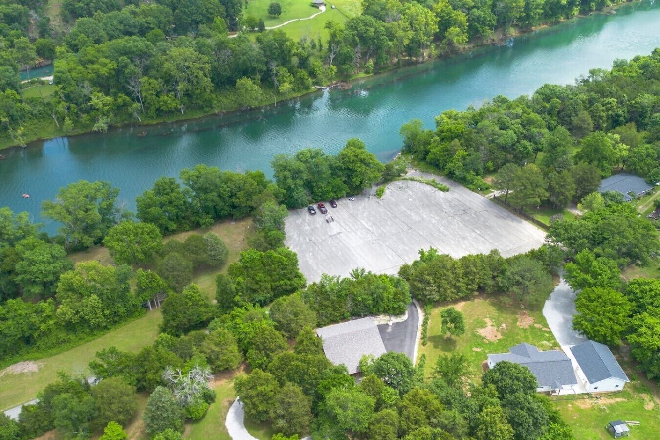 An aerial view of a property with a large open area, a body of water, and surrounding greenery.