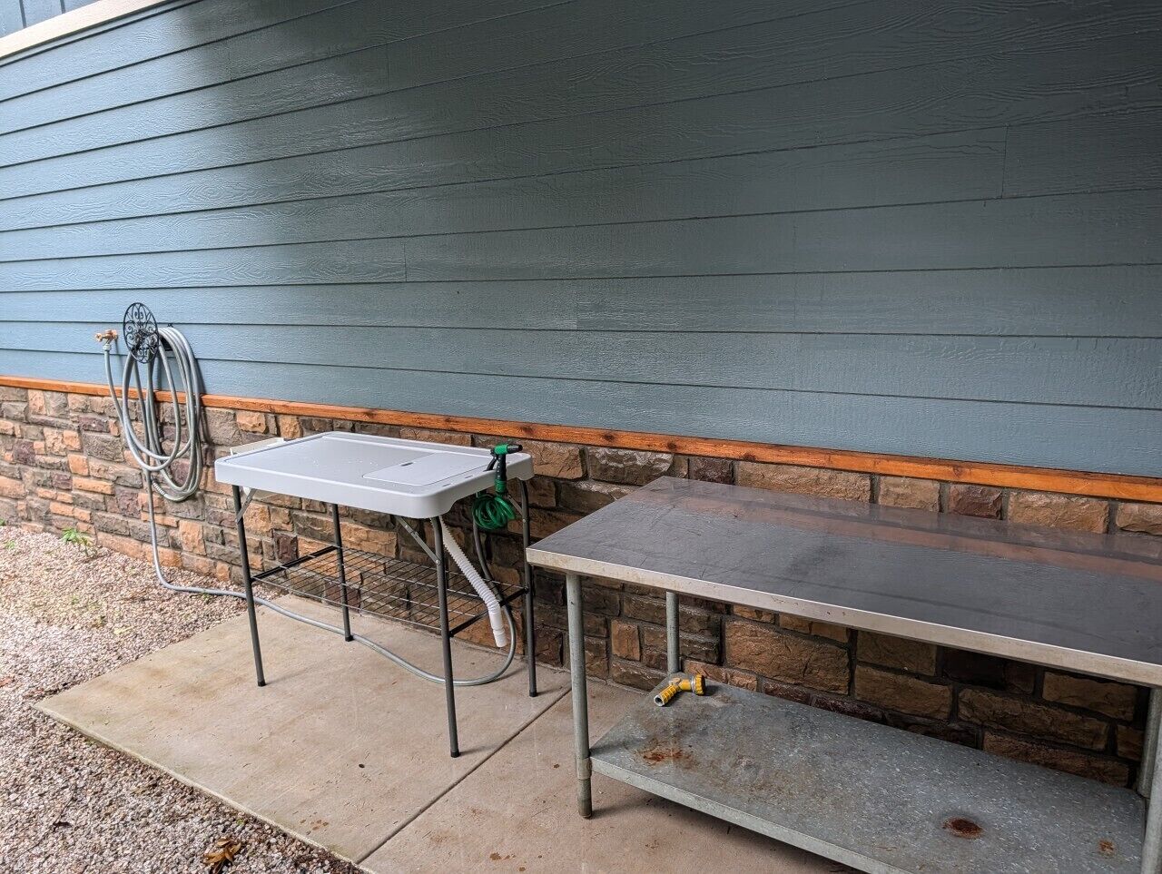 A concrete outdoor table with a metal frame and a white sink, positioned against a stone wall with a wooden ledge.