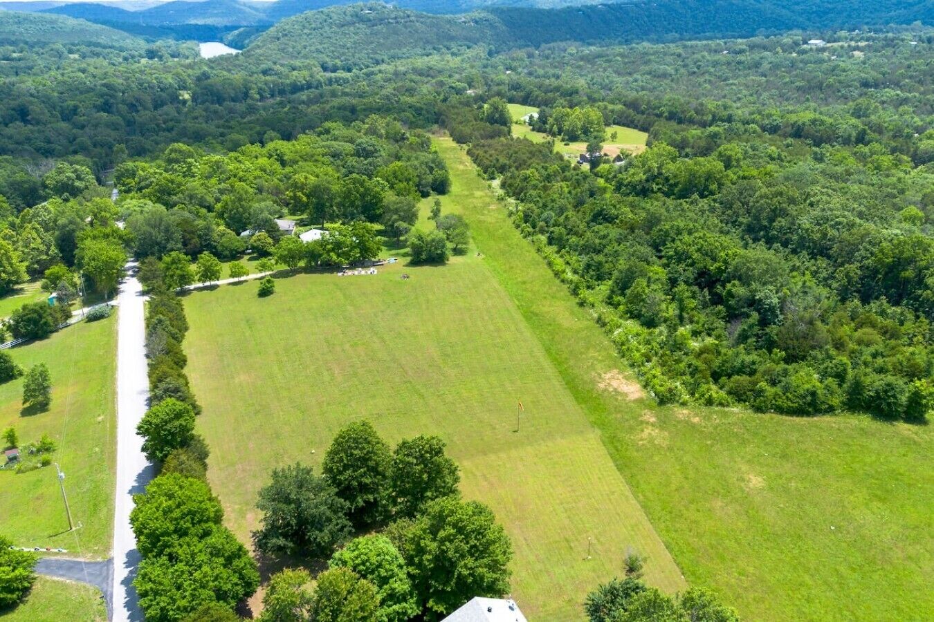 Luchtbeeld van een landelijk gebied met een groot groen veld, een kronkelende weg en verspreide gebouwen.