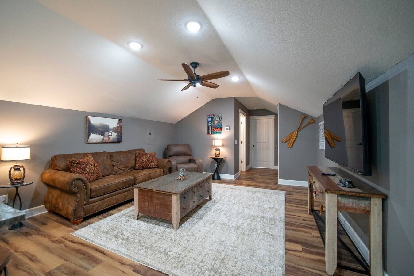 Ein Wohnzimmer mit braunem Ledersofa, einem Holztisch, Deckenventilator, Fernseher und Kamin.