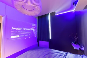 Een moderne slaapkamer met een bed, een aan de muur bevestigde projector die een film toont, en een plafondlamp.