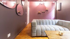 Ein modernes Wohnzimmer mit einem grauen Sofa, einem Holztisch, einem Spiegel und Wandregalen mit Blumen.