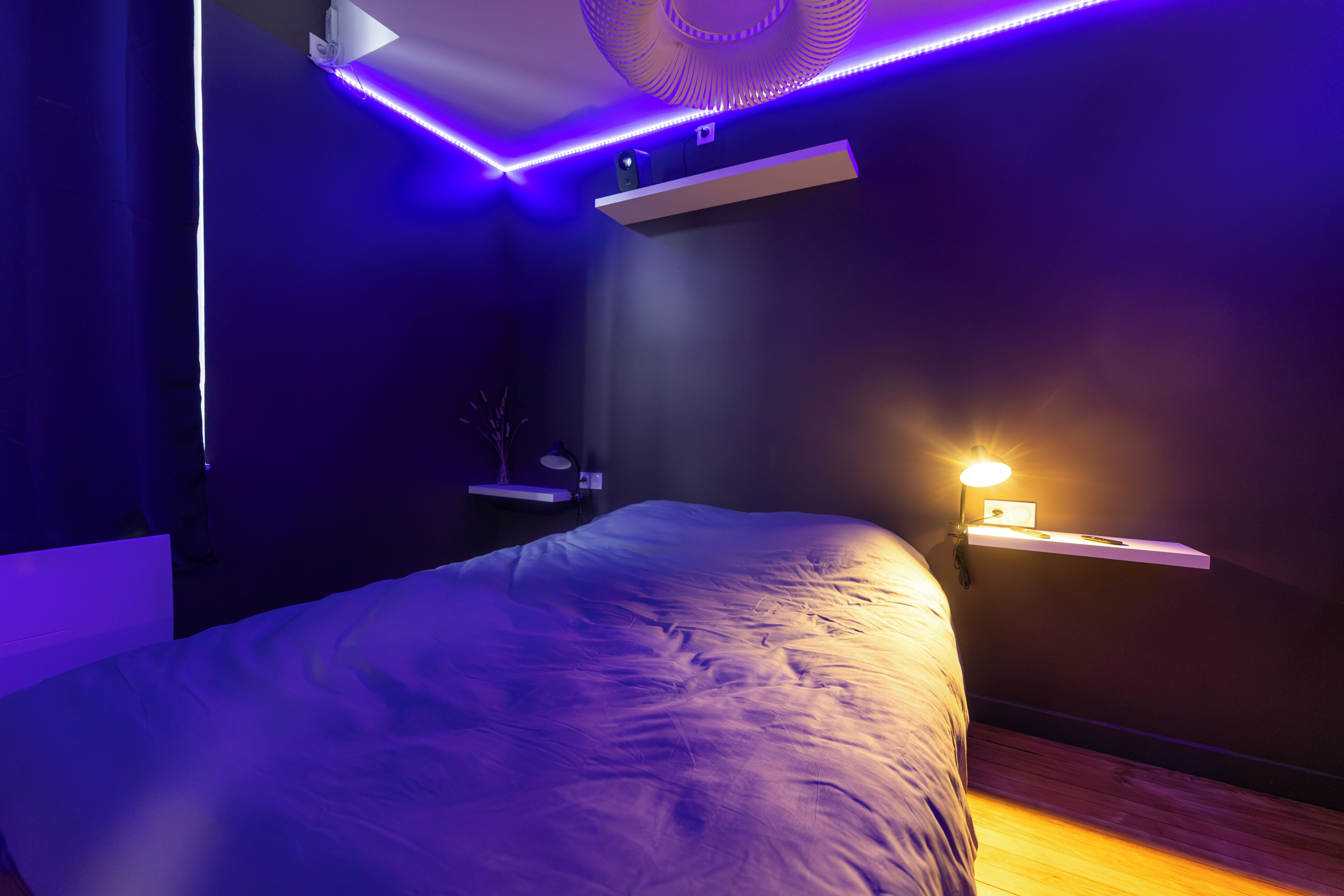 A modern bedroom with a bed, a shelf, a wall-mounted light, and a ceiling light fixture.