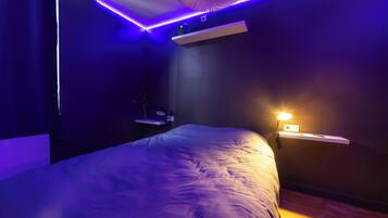 A modern bedroom with a bed, a shelf, a wall-mounted light, and a ceiling light fixture.
