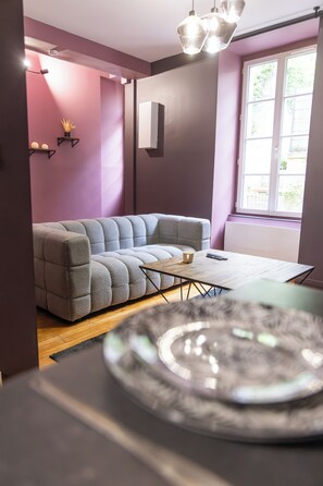 Een moderne woonkamer met een hoekbank, een kleine houten tafel en een groot raam met natuurlijk licht.