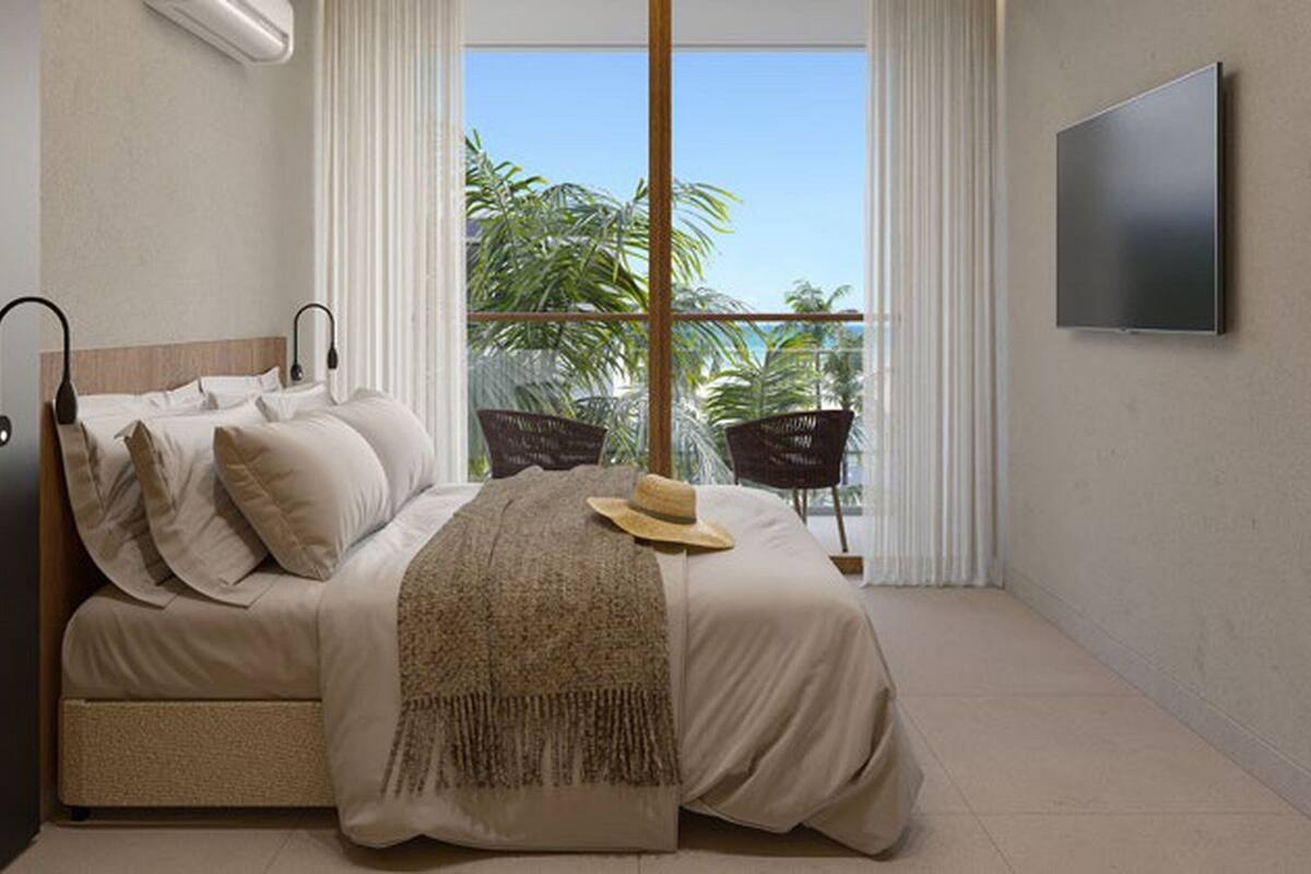 Une chambre avec un lit, une télévision, une fenêtre donnant sur des palmiers et un balcon avec des chaises.