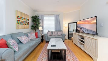Een woonkamer met een bank, een salontafel, een televisie en een schilderij aan de muur.