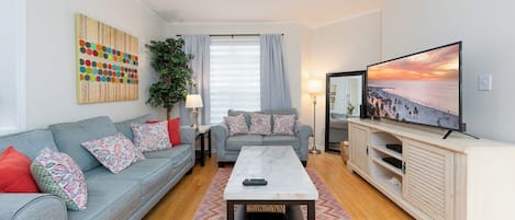 A living room with a sofa, a coffee table, a TV, and a painting on the wall.