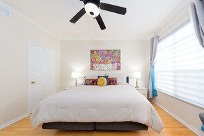 A bedroom with a bed, ceiling fan, artwork, bedside lamps, and a window with curtains. - Beautiful Quiet Condo in Clearwater, Florida (Clearwater)