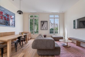 Ein modernes Wohnzimmer mit einem Holzes Esstisch, einer Couch und einem an der Wand befestigten Fernseher.
