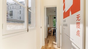 Un couloir doté d’un plancher en bois, un coin repas avec une table et des chaises, et une fenêtre donnant sur un immeuble.