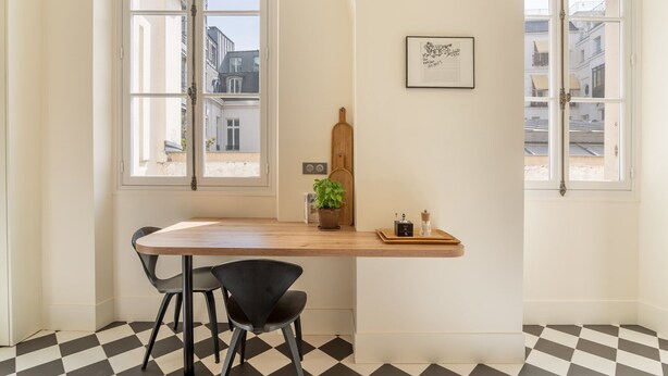 Une pièce avec une table en bois, deux chaises noires, une plante en pot, un certificat encadré et un sol à carreaux.