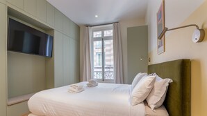 Une chambre d’hôtel équipée d’un lit, d’un téléviseur à écran plat, d’une fenêtre avec des rideaux et d’un luminaire fixé au mur.