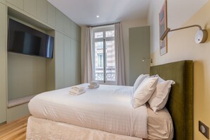 Ein Hotelzimmer mit Bett, Flachbildfernseher, Fenster mit Vorhängen und einer Wandleuchte.