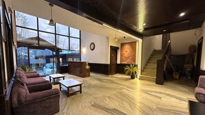 Un amplio vestíbulo con mostrador de recepción, zona de estar, ventanas grandes y una escalera.