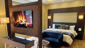 Una habitación de hotel moderna con televisión, cama, sofá, mesita y lámpara.