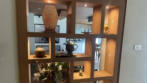 Una pantalla montada en la pared con diversos objetos decorativos, incluyendo un jarrón grande, una tetera y una pequeña mesa con una lámpara.