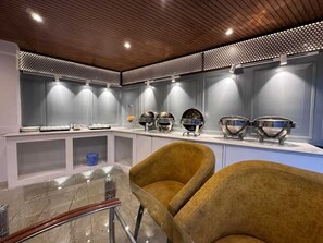 A modern kitchen with a central island, overhead lighting, and a seating area with chairs. - Hotel Golden bees gym & spa (Srinagar)
