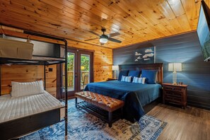 Een slaapkamer met een stapelbed, een enkel bed, een plafondventilator, een nachtkastje en een groot raam.