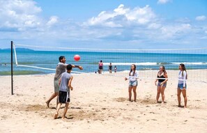 Partita di beach volley con giocatori e spettatori su una spiaggia sabbiosa.