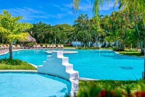 Una piscina con una scala bianca che vi si apre, circondata da palme e poltroncine da relax.