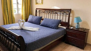 Ein ordentlich bezogenes Bett mit blauer Steudecke, zwei Kissen und einer dekorativen Schwanen-Handtuch-Arrangement.