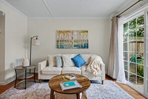 Ein Wohnzimmer mit Sofa, Couchtisch, einem Gemälde und Blick durch ein Fenster.