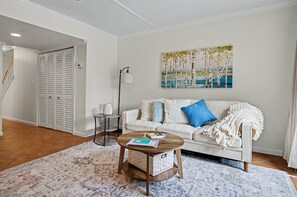 Ein Wohnzimmer mit einem weißen Sofa, einem Couchtisch, einem Bild an der Wand und einer Treppe im Hintergrund.