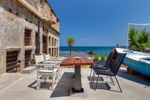 An outdoor seating area with a table and chairs, a view of the sea, and a boat. - Skiff - Transformed Studio Sea View (Chania)