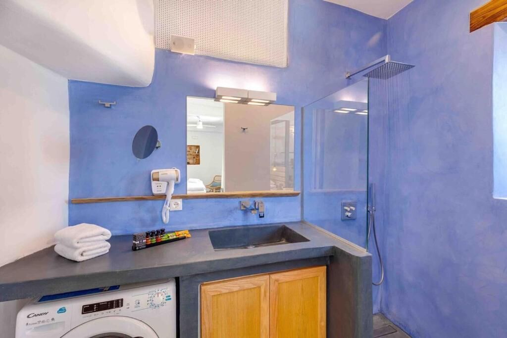A bathroom with a blue wall, a sink, a mirror, a shower, and a washing machine.