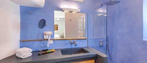 A bathroom with a blue wall, a sink, a mirror, a shower, and a washing machine.