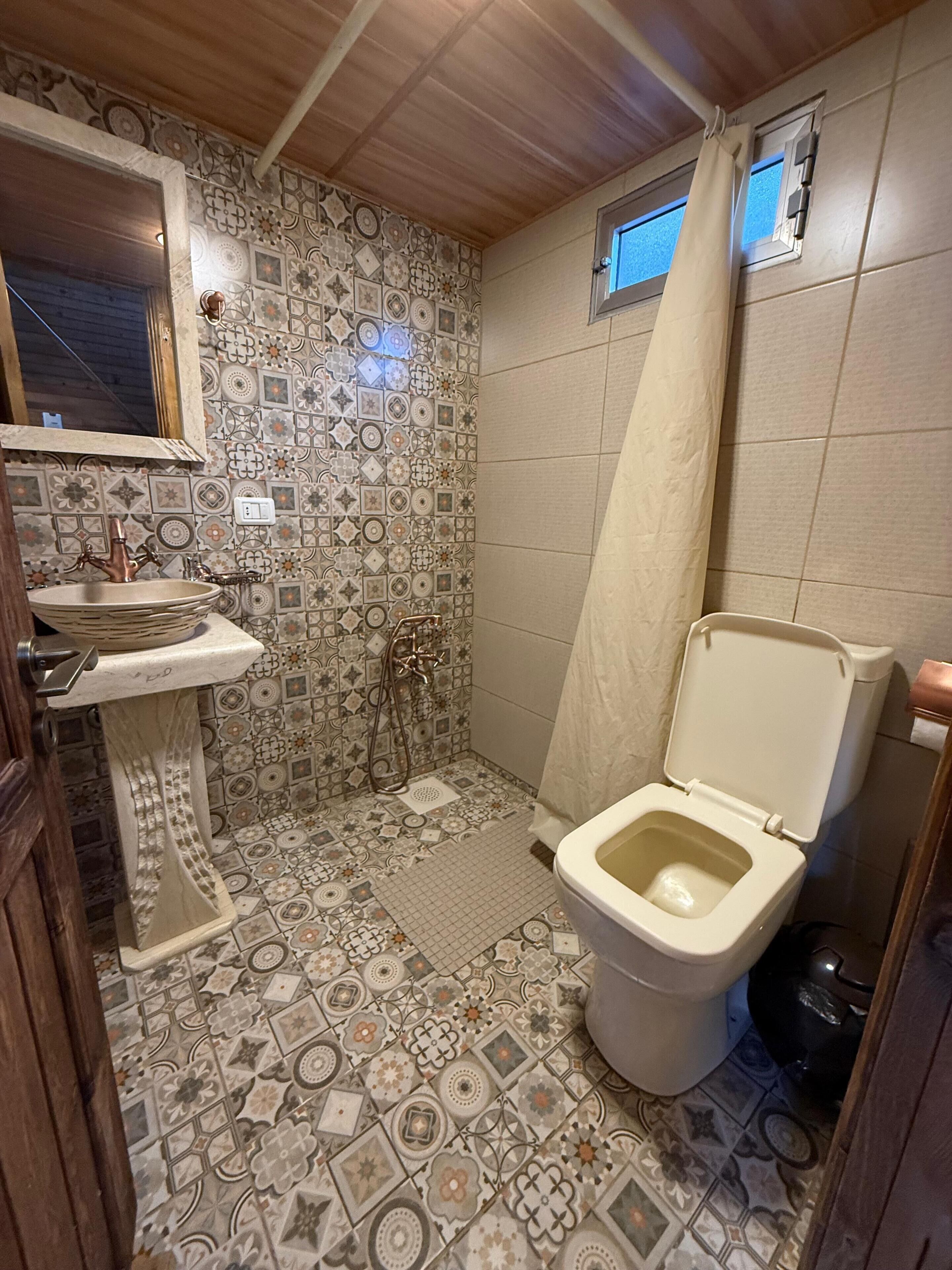 A bathroom with a patterned tile floor, a sink, a toilet, and a shower.
