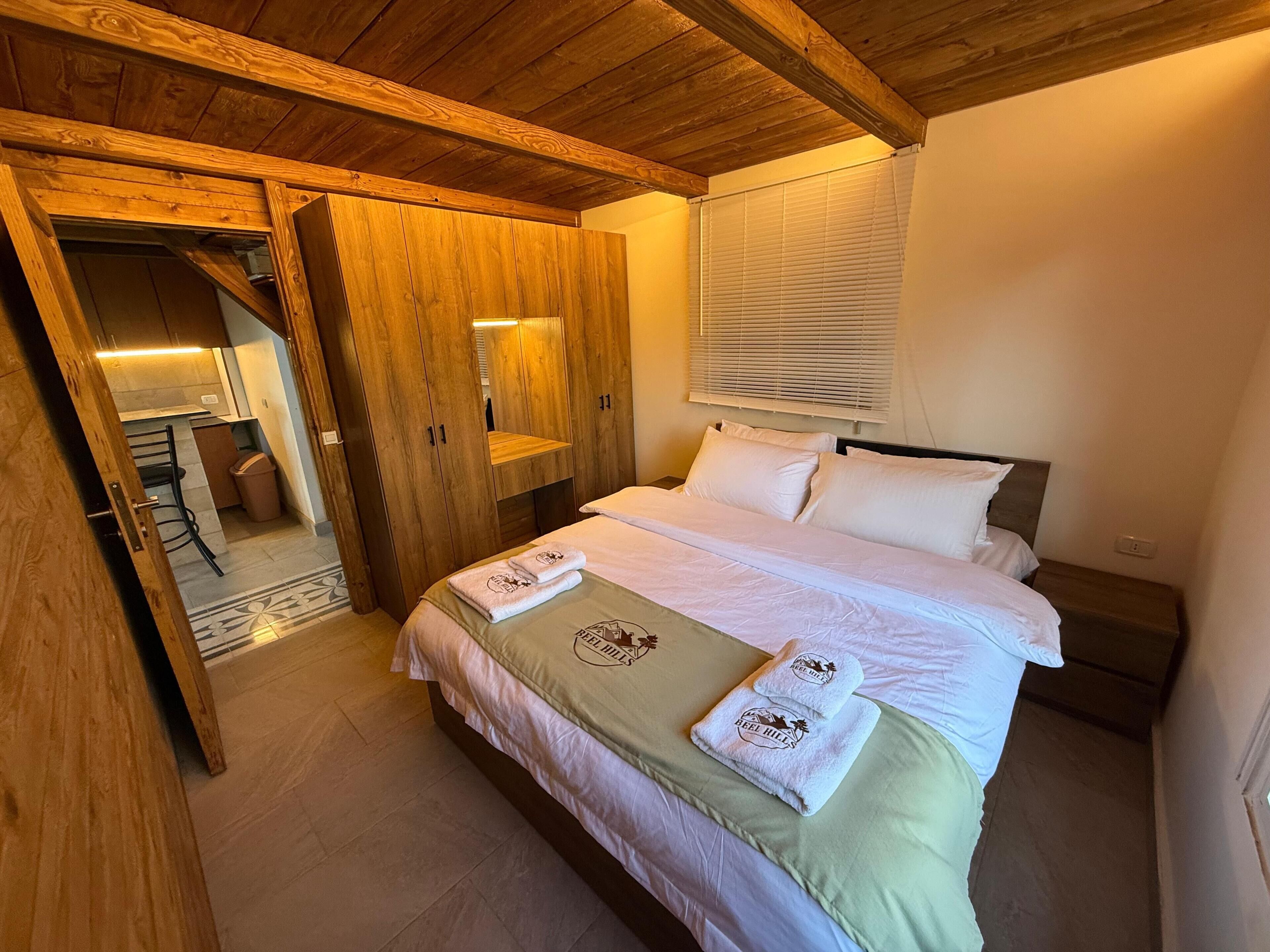 A bedroom with a bed, wooden wardrobe, and a bathroom visible through an open door.