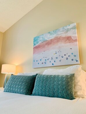 Ein Hotelzimmer mit Bett, Kissen, einem Wandbild und einer Nachttischlampe.