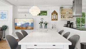 A modern kitchen with white cabinetry, a large dining table, and a view of greenery through a window. - "Stig" - 1.1km from the sea by Interhome (Hornbæk)