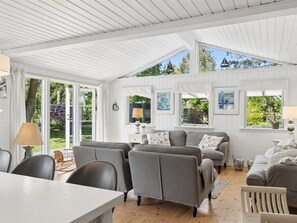 Ein geräumiges Zimmer mit hoher Decke, großen Fenstern und einer gemütlichen Sitzecke mit Sofa und Sesseln.