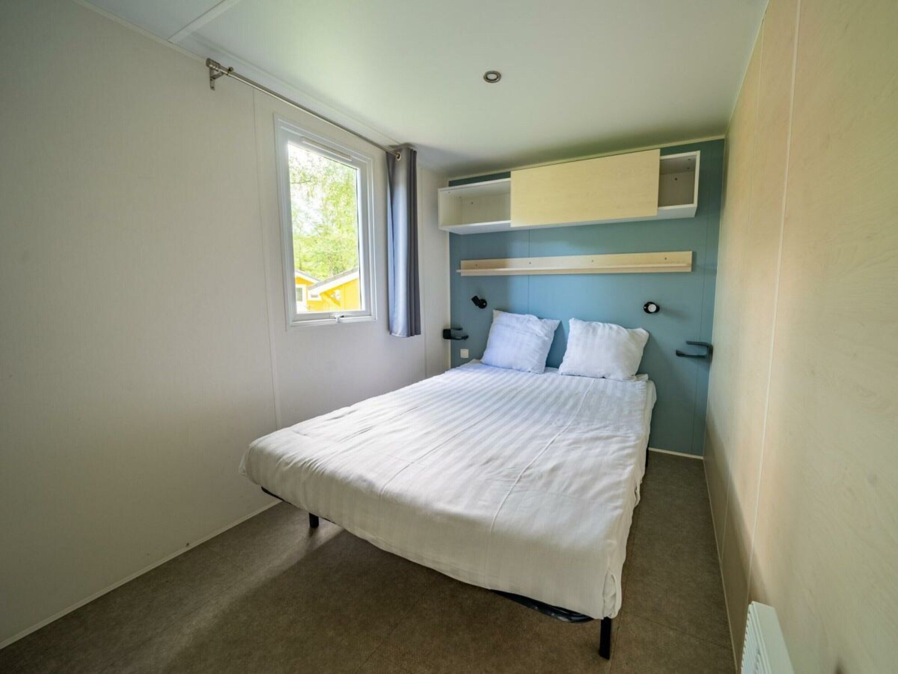 A bedroom with a bed, a window, a built-in shelf, and a radiator.