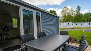 A patio with a table and chairs, a sliding glass door leading to a kitchen, and a view of a row of mobile homes in the background. - Holiday Home in Amstelveen With Terrace (Amstelveen)