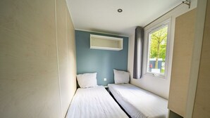 A small, single-room accommodation with two beds, a window with curtains, and a wall-mounted air conditioning unit. - Holiday Home in Amstelveen With Terrace (Amstelveen)