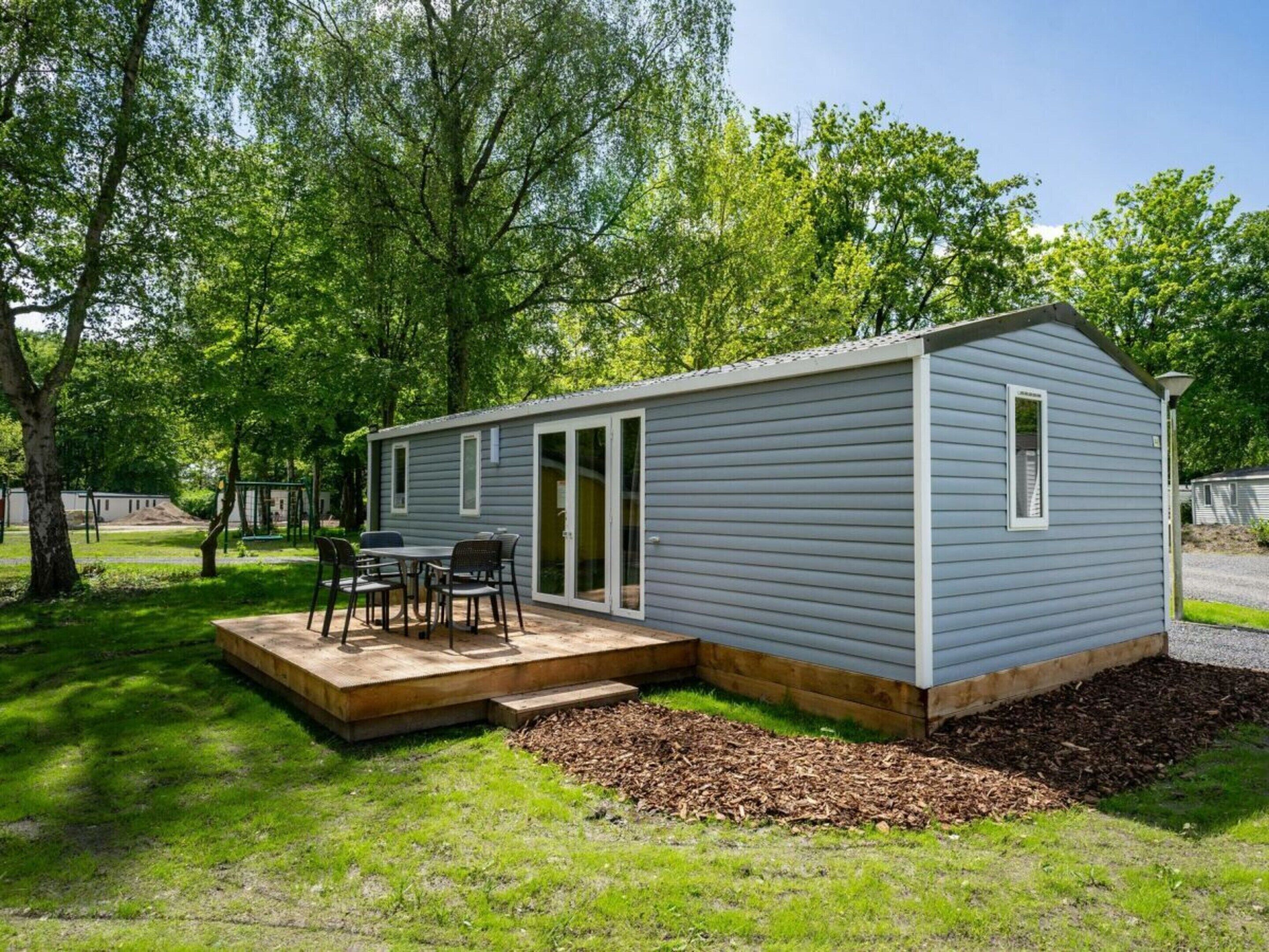 Una casa móvil de un piso con un patio, una pequeña terraza y un área de estar al aire libre techada.